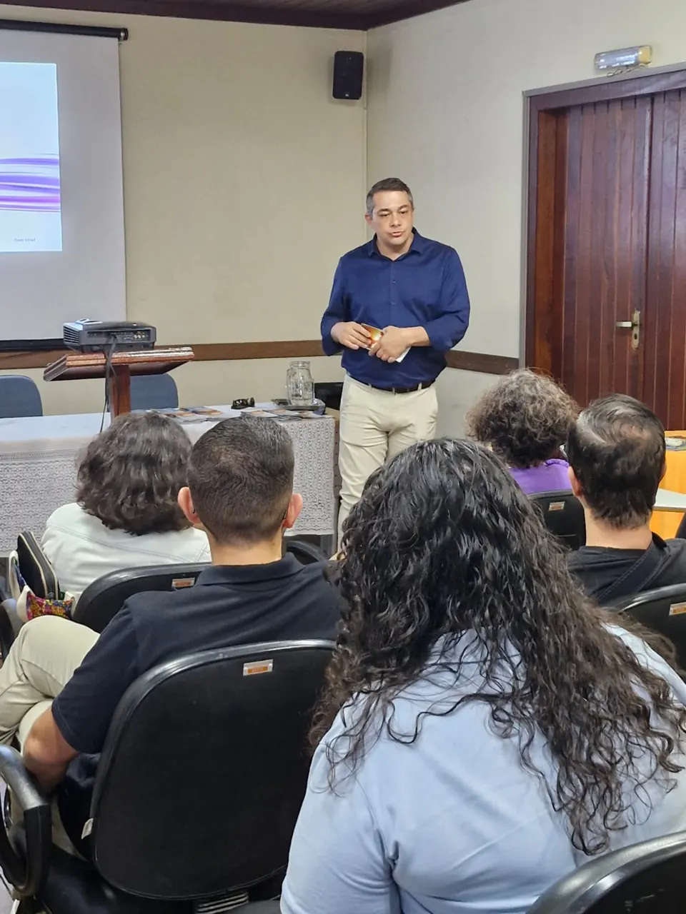 Palestrante de camisa azul conduzindo a apresentação para a plateia